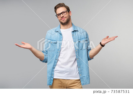 Portrait of confused clueless young man in jeans shirt standing over grey background Portrait of confused clueless young man in jeans shirt standing over grey background 73587531