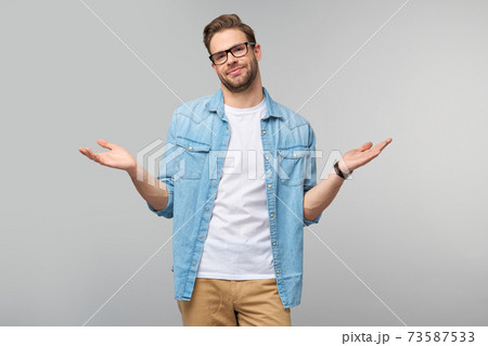 Portrait of confused clueless young man in jeans shirt standing over grey background Portrait of confused clueless young man in jeans shirt standing over grey background 73587533