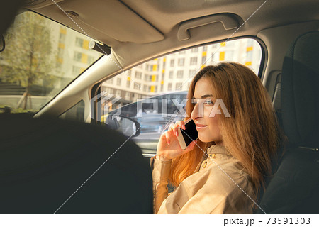 Young woman talking on the phone while sitting on the front passenger seat of the car against the background of high-rise buildings Young woman talking on the phone while sitting on the front passenger seat of the car against the background of high-rise buildings 73591303
