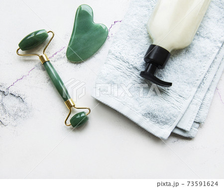 Face massage jade roller with cosmetic product on white marble background Face massage jade roller with cosmetic product on white marble background 73591624
