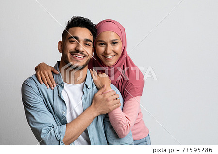 Portrait of romantic smiling muslim couple posing over grey studio background 73595286