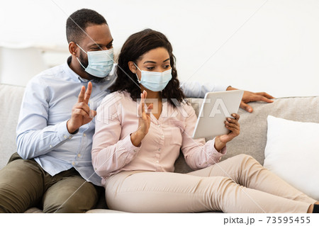 Black couple in masks waving to tablet during videocall 73595455