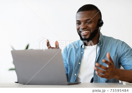 Video Conference. Cheerful african american man in headset making web call on laptop Video Conference. Cheerful african american man in headset making web call on laptop 73595484