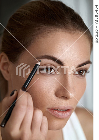 Eyebrows shaping. Beauty young woman with brow pencil. Closeup of beautiful girl with professional makeup contouring brows with eyebrow pencil. Eyebrows shaping. Beauty young woman with brow pencil. Closeup of beautiful girl with professional makeup contouring brows with eyebrow pencil. 73596404