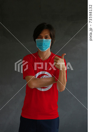 Man wearing hygienic mask and wearing Tunisia flag colored shirt and cross one s arm with thumbs up 73598132