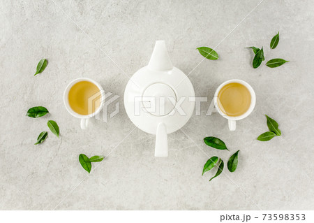 Herbal tea with two white tea cups and teapot, with green tea leaves. Flat lay, top view. Tea concept Herbal tea with two white tea cups and teapot, with green tea leaves. Flat lay, top view. Tea concept 73598353