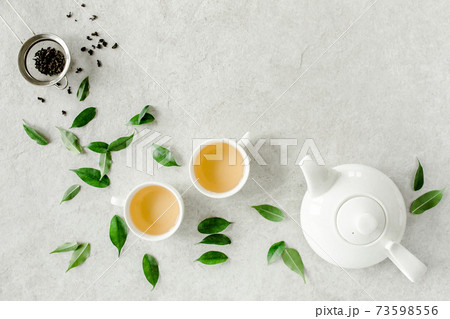 Herbal tea with two white tea cups and teapot, with green tea leaves. Flat lay, top view. Tea concept 73598556