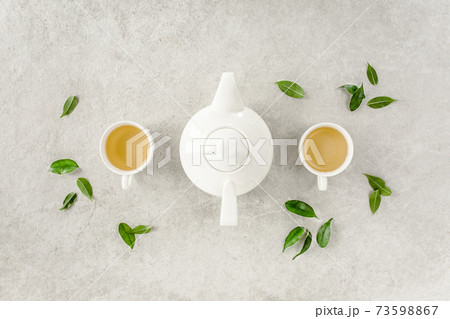 Herbal tea with two white tea cups and teapot, with green tea leaves. Flat lay, top view. Tea concept Herbal tea with two white tea cups and teapot, with green tea leaves. Flat lay, top view. Tea concept 73598867