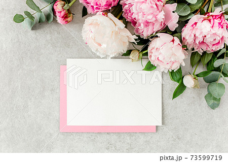 Mockup invitation, blank paper greeting card, pink envelope and peonies on gray stone table. Flower background. Flat lay, top view. Mockup invitation, blank paper greeting card, pink envelope and peonies on gray stone table. Flower background. Flat lay, top view. 73599719