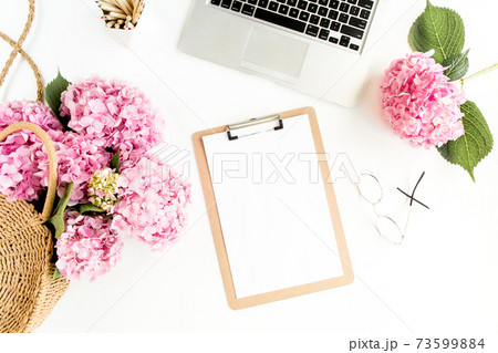 Stylized women's desk. Workspace with clipboard, laptop, bouquet hydrangea, accessories on white background. Flat lay. Top view. Stylized women's desk. Workspace with clipboard, laptop, bouquet hydrangea, accessories on white background. Flat lay. Top view. 73599884