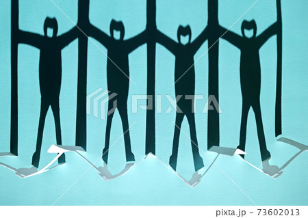 新型コロナ対策で衝立を挟んで繋がる人々の切り紙の影。青い背景。 73602013