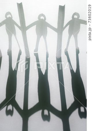 新型コロナ対策で衝立を挟んで繋がる人々の切り紙と影。白い背景。 73602019