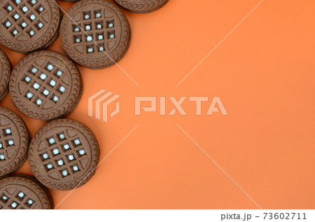 Detailed picture of dark brown round sandwich cookies with coconut filling on an orange surface. Background image of a close-up of several treats for tea 73602711
