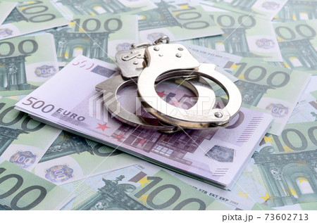 Police handcuffs lies on a set of green monetary denominations of 100 euros. A lot of money forms an infinite heap 73602713