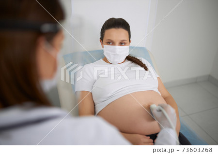 Pregnant woman in mask having ultrasound screening Pregnant woman in mask having ultrasound screening 73603268