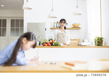 リビングで勉強する子供をキッチンで見守る母親 73609376