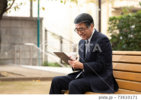 ベンチに座ってタブレットを操作するシニア男性 73610171