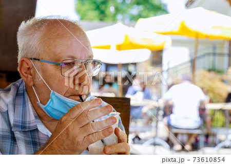 Old man in medical face mask are a drinks water in a summer cafe coronavirus covid-19 Old man in medical face mask are a drinks water in a summer cafe coronavirus covid-19 73610854