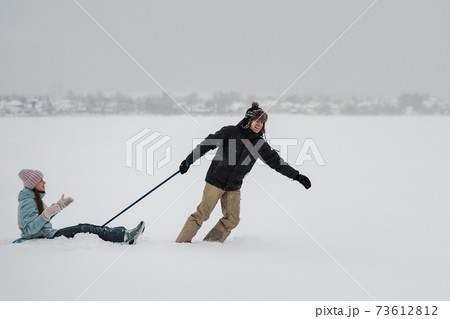 Man pulling snow tube with girlfriend. Young happy couple walking in winter day 73612812