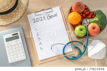 2021 New Year Goals in new normal lifestyle, work-life balance with face mask safety from covid-19, healthy food, cholesterol diet, good heart health, blank resolution list on white paper medical note 73613048