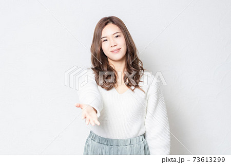 白い壁の前に立って、手を差し出す女性 73613299