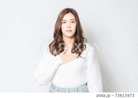 白い壁の前に立って胸に手を当てる若い女性 73613973