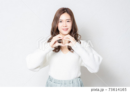 白い壁の前に立って、手でハートの形を作る若い女性 白い壁の前に立って、手でハートの形を作る若い女性 73614165