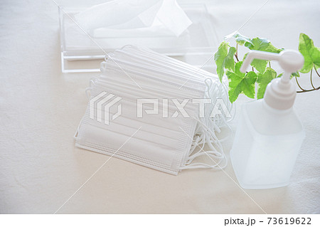 たくさんの不織布マスクの束とアルコールボトル、ティッシュペーパー 73619622