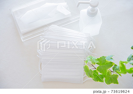 たくさんの不織布マスクの束とアルコールボトル、ティッシュペーパー 73619624