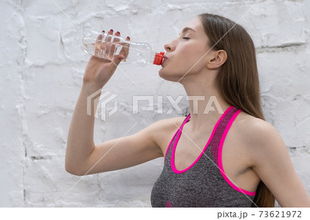 Young athlete woman takes a break drinking water from plastic bottle. Young woman drinking water after working out in the gym, health and sport concept 73621972
