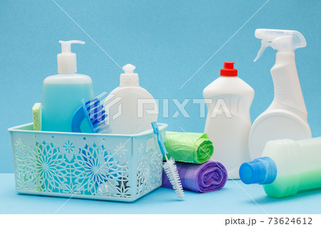Bottles of dishwashing liquid in basket, sponges and brushes on blue background. 73624612