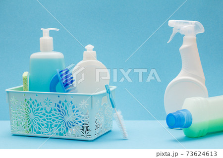 Bottles of dishwashing liquid in basket, sponges and brushes on blue background. 73624613