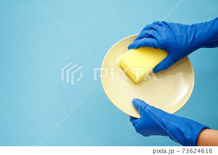 Women's hands in protective gloves with sponge and plate on blue background. Women's hands in protective gloves with sponge and plate on blue background. 73624616