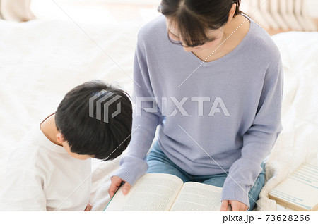 ベッドの上に座って本を読む子供と母親の写真素材
