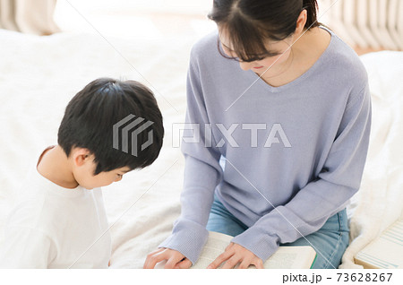 ベッドの上に座って本を読む子供と母親の写真素材