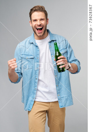 Young Man holding wearing jeans shirt holding Bottle of beer standing over Grey Background Young Man holding wearing jeans shirt holding Bottle of beer standing over Grey Background 73628367