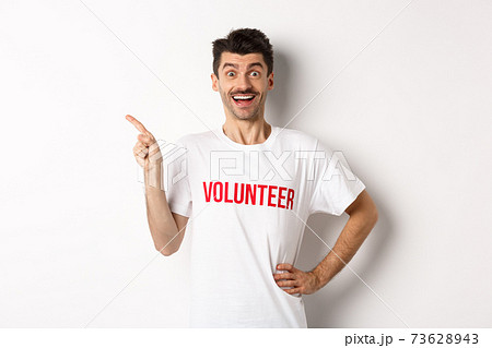 Happy smiling volunteer pointing finger left at copy space, showing announcement, white background Happy smiling volunteer pointing finger left at copy space, showing announcement, white background 73628943