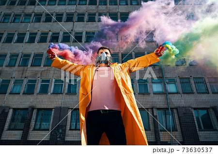Young man in respirator mask hold smoke bombs in raised hands Young man in respirator mask hold smoke bombs in raised hands 73630537