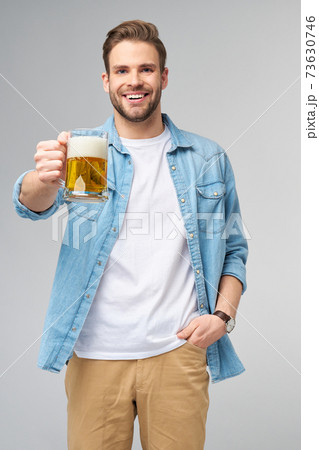 Young Man holding wearing jeans shirt holding glass of beer standing over Grey Background 73630746