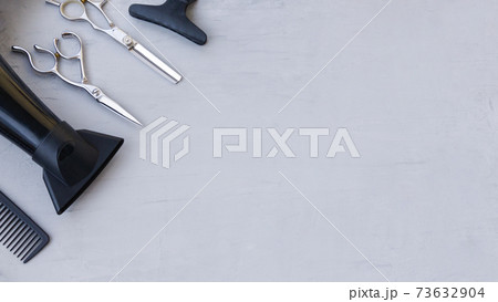 Hairdressing tools in the corner on a light gray background with space for text. Hair salon accessories, scissors, hair dryer and comb. 73632904