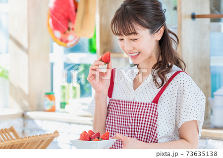 キッチンでイチゴをつまみ食いする女性の写真素材