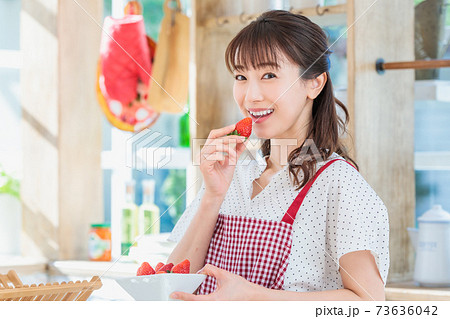 キッチンでイチゴをつまみ食いする女性の写真素材