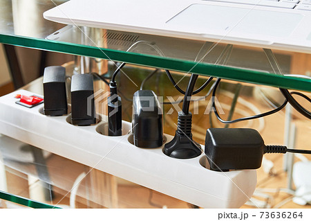 Electrical power strip overloaded with multiple electrical cords plugged in. Many plugs plugged into electric power bar 73636264