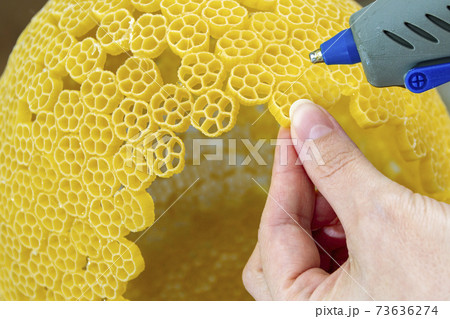 Woman glues pasta with a hot glue gun during the manufacture of crafts Woman glues pasta with a hot glue gun during the manufacture of crafts 73636274