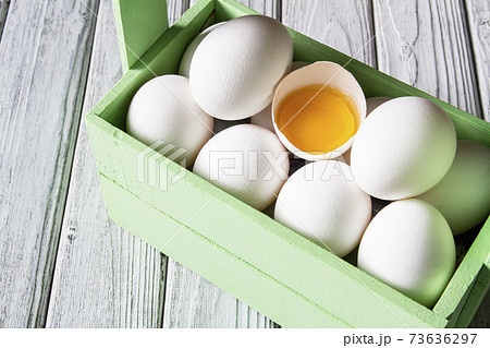 Close-up of fresh white organic chicken eggs and egg yolk in the green wooden box on light wooden background 73636297