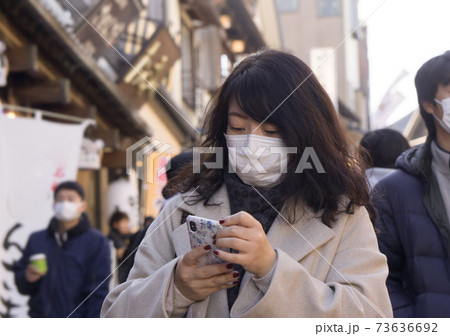 マスクをつける女性がスマホを操作する 73636692