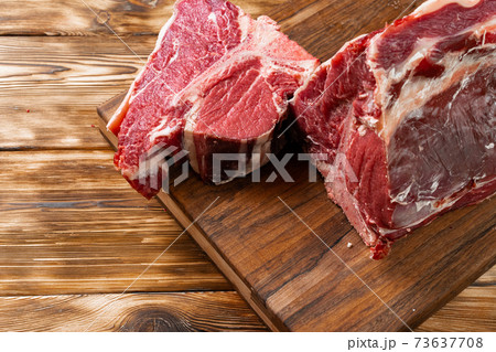 Raw T-bone steak with herbs on wooden board Raw T-bone steak with herbs on wooden board 73637708