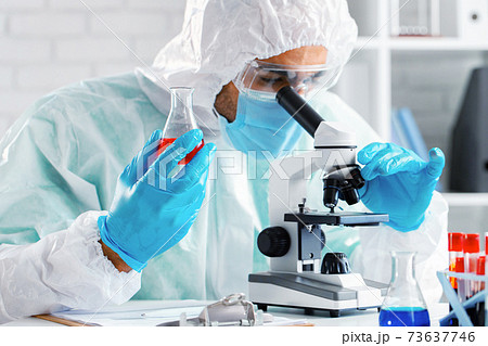 Medical worker in protective gown looking in microscope 73637746