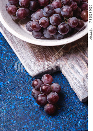 Fresh ripe grape berries in white wooden bowl and old cutting board on blue abstract background, angle view macro Fresh ripe grape berries in white wooden bowl and old cutting board on blue abstract background, angle view macro 73638939