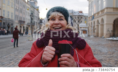 Senior woman grandmother tourist smiling, showing thumb up in winter city center of Lviv, Ukraine Senior woman grandmother tourist smiling, showing thumb up in winter city center of Lviv, Ukraine 73640754